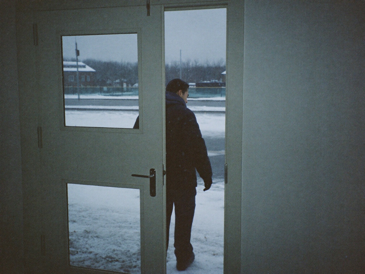 A man stepping out of a building through a glass door onto a snowy sidewalk